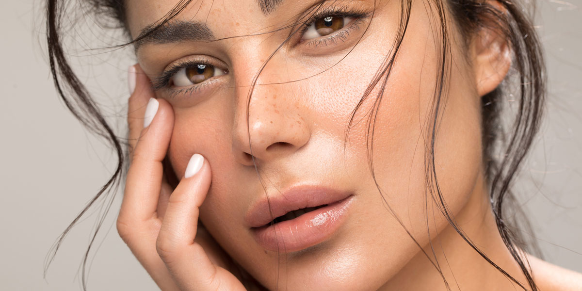 Close up of woman touching cheek with dewy radiant skin
