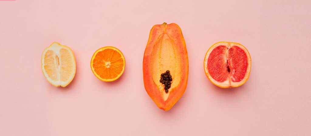 halved citrus fruits and papaya arranged in a row on a pink background