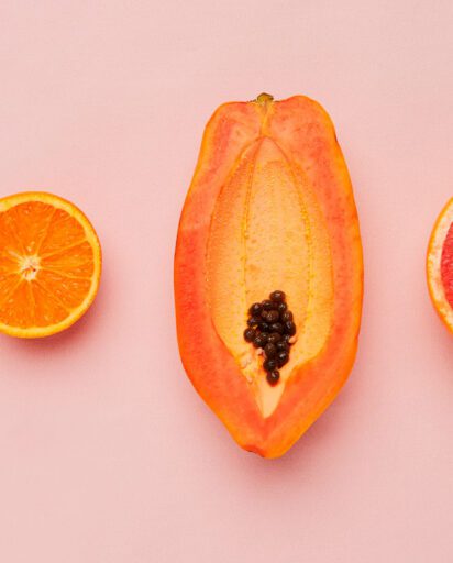 halved citrus fruits and papaya arranged in a row on a pink background