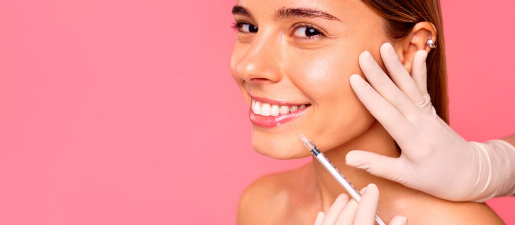 smiling-woman-receiving-a-cosmetic-injection-in-her-cheek-against-a-pink-background