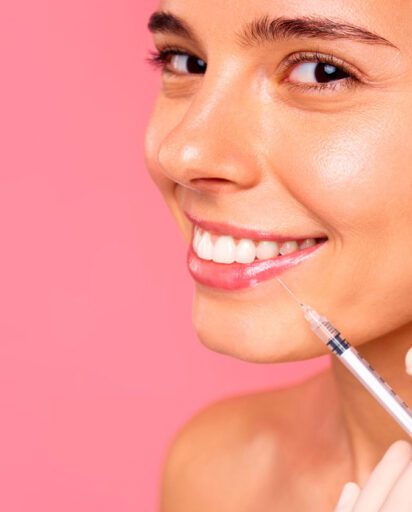 smiling-woman-receiving-a-cosmetic-injection-in-her-cheek-against-a-pink-background
