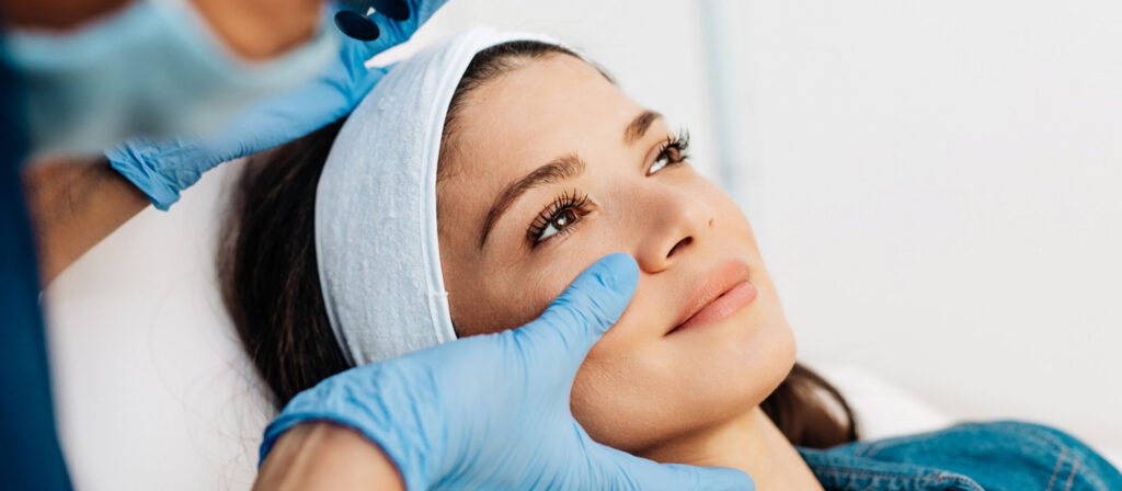 woman-in-a-headband-lying-back-while-a-gloved-provider-examines-her-face