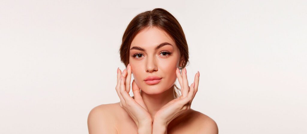 woman-resting-her-hands-along-her-jawline-against-a-plain-background