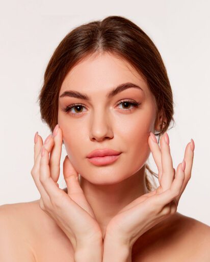 woman-resting-her-hands-along-her-jawline-against-a-plain-background