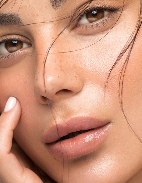Close up of woman touching cheek with dewy radiant skin