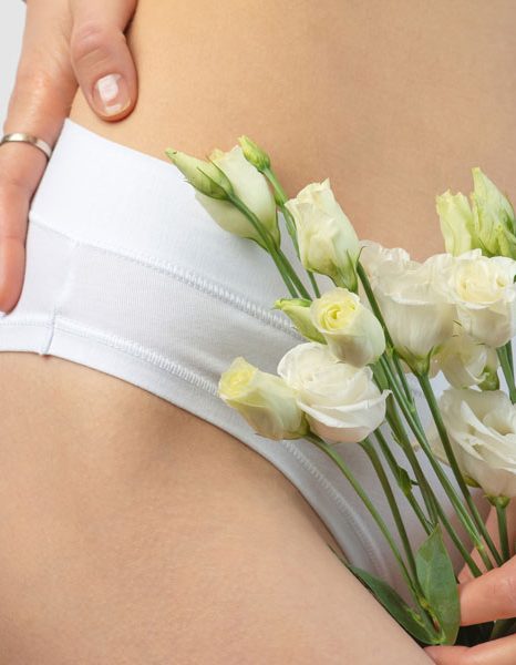 Woman holding flowers near lower abdomen in underwear